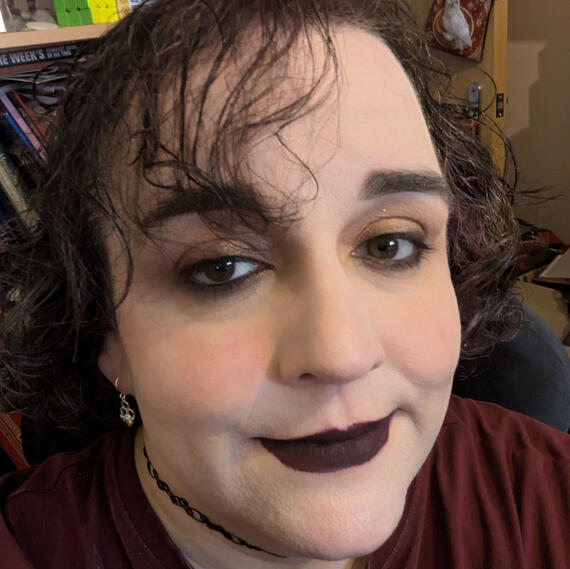 Picture of Alyssa's face, dark brown curly hair with purple highlights, soft smoky eyeshadow, dark plum lips.